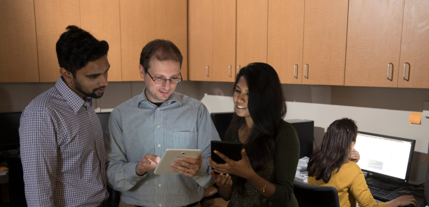 Graduate student Phani Vadrevu, professor Roberto Perdisci and graduate student Karthika Subramani review data on a tablet device while graduate student Roxana Attar works in the laboratory