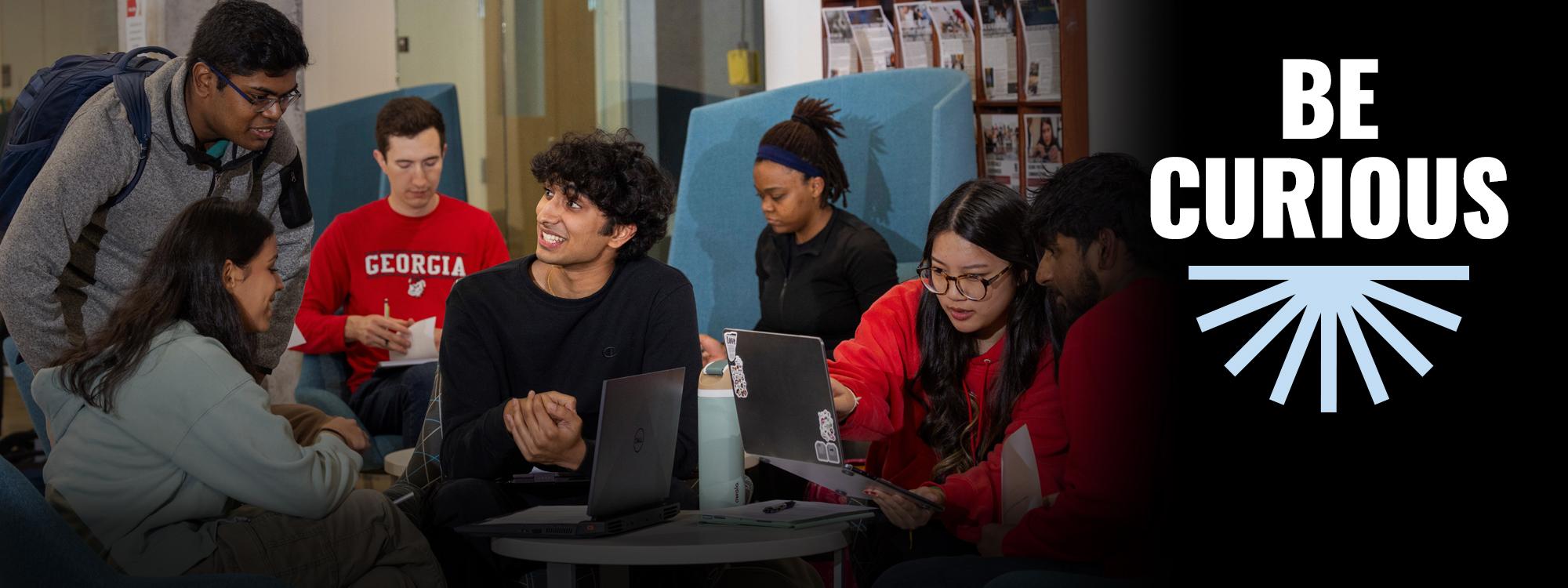 Be Curiou text. Several students looking at laptops, discussing Computer Science